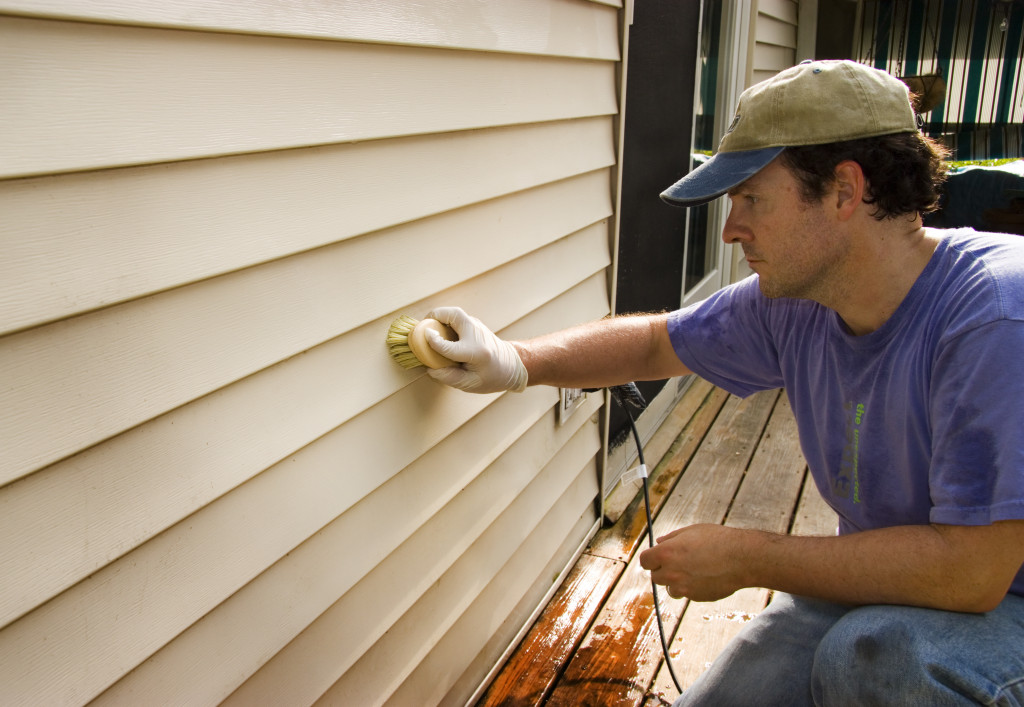 A man washing vinyl siding by hand with a brush