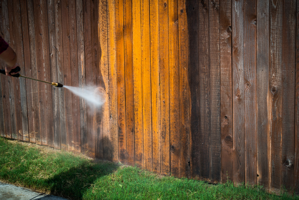 A person pressure washing a wooden fence