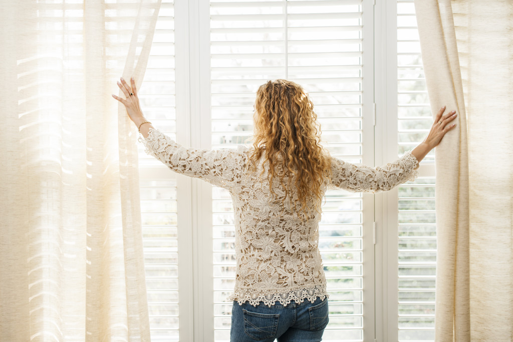 woman opening window curtains