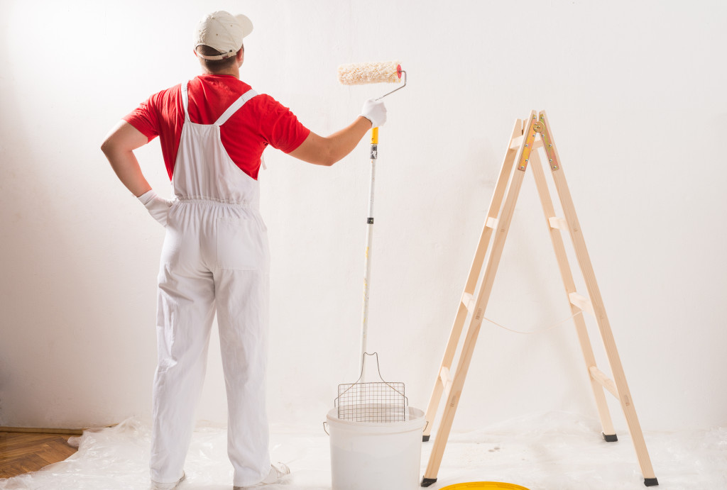 male painter looking at newly painted white wall with ladder on the side