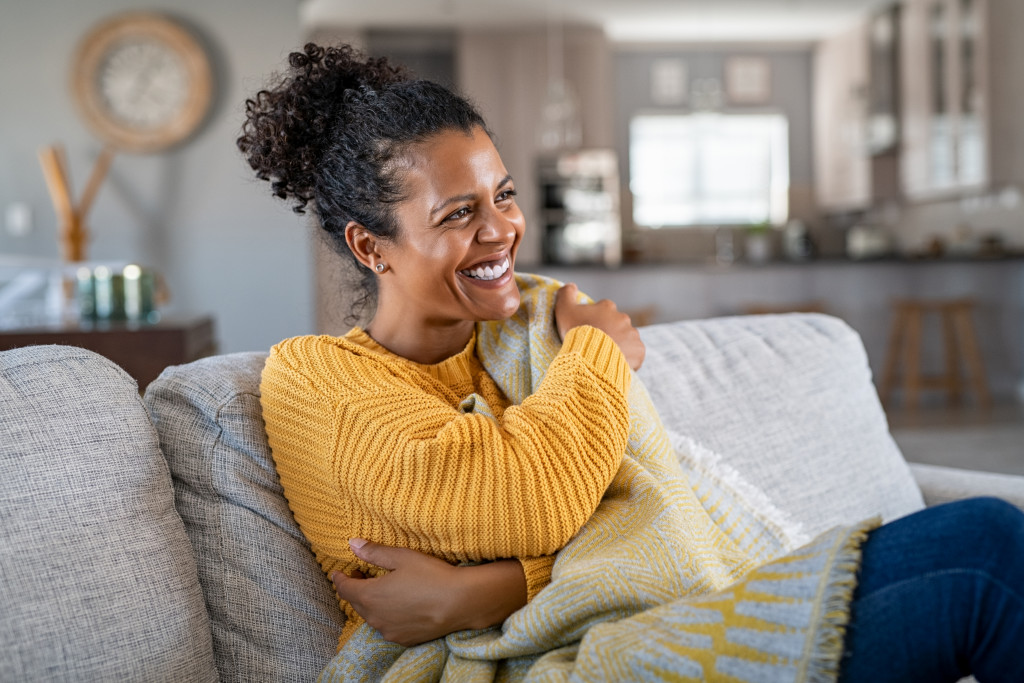 Young woman sitting on a sofa while holding a blanket at home.